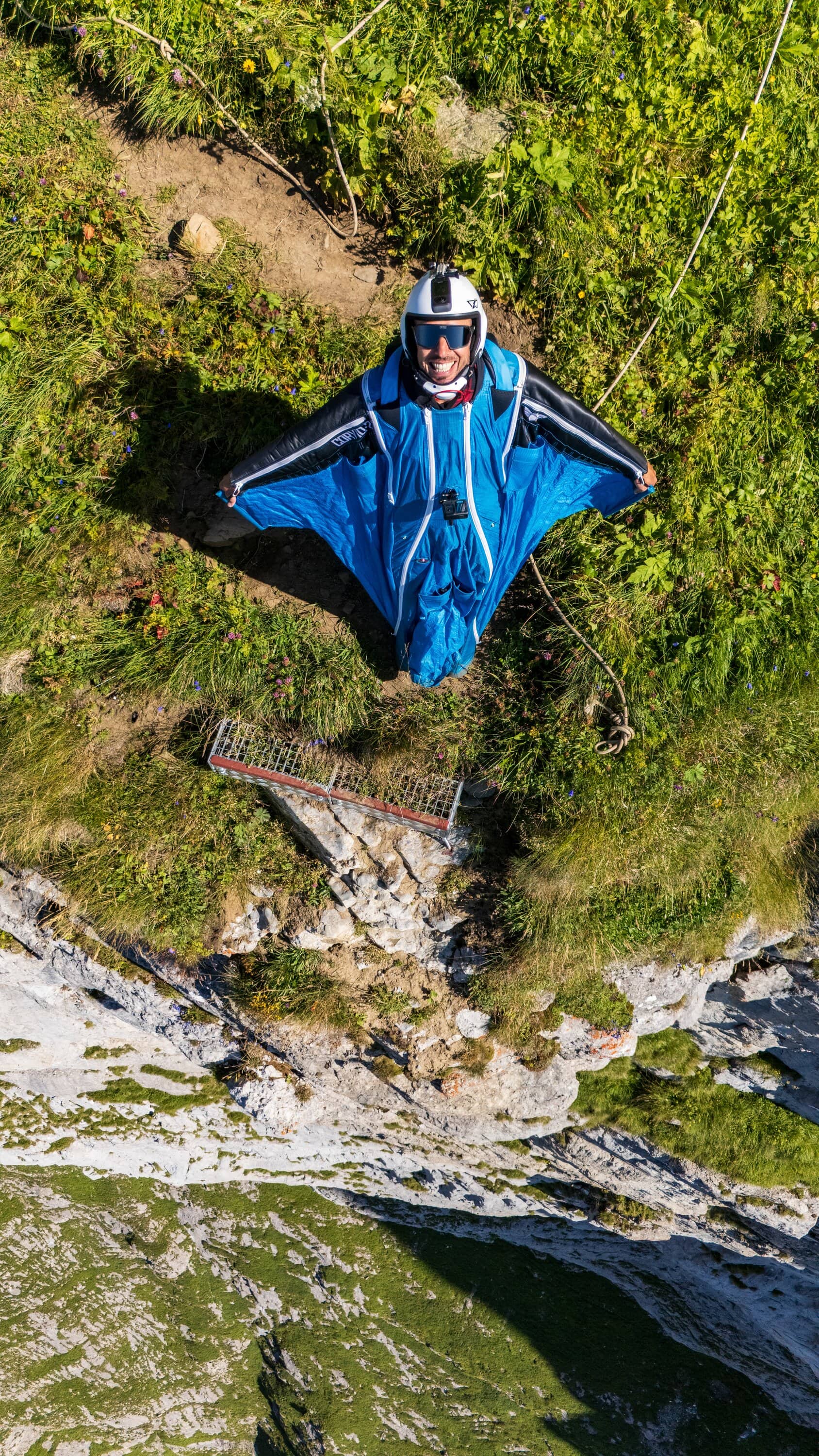 Wingsuit-Pilot steht auf einem grasigen Absprunghang