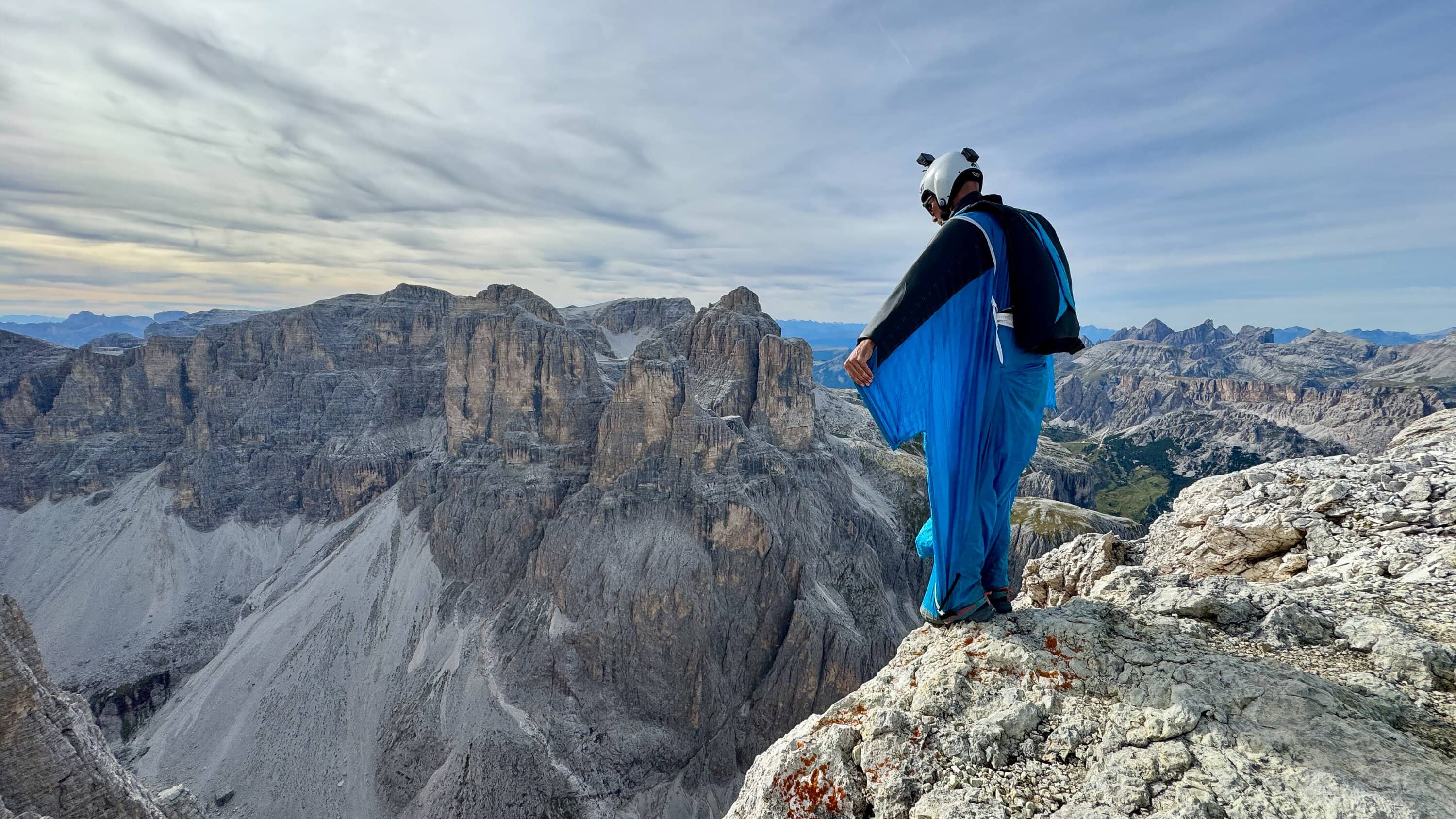 Wingsuit-Pilot steht auf einem Felsgipfel über alpinen Bergen