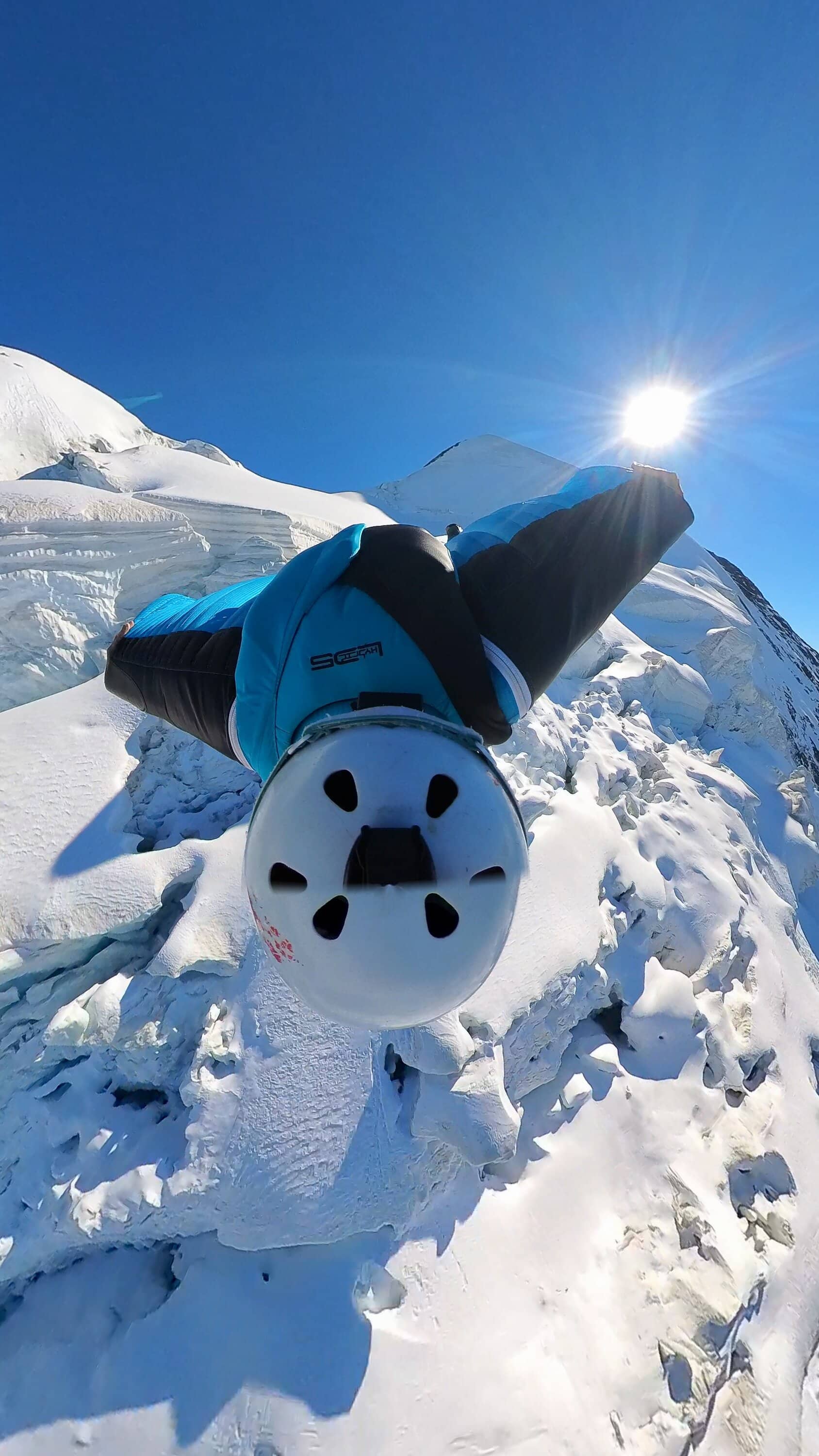 Blauer Wingsuit und Helm im Schnee neben einem Berggrat
