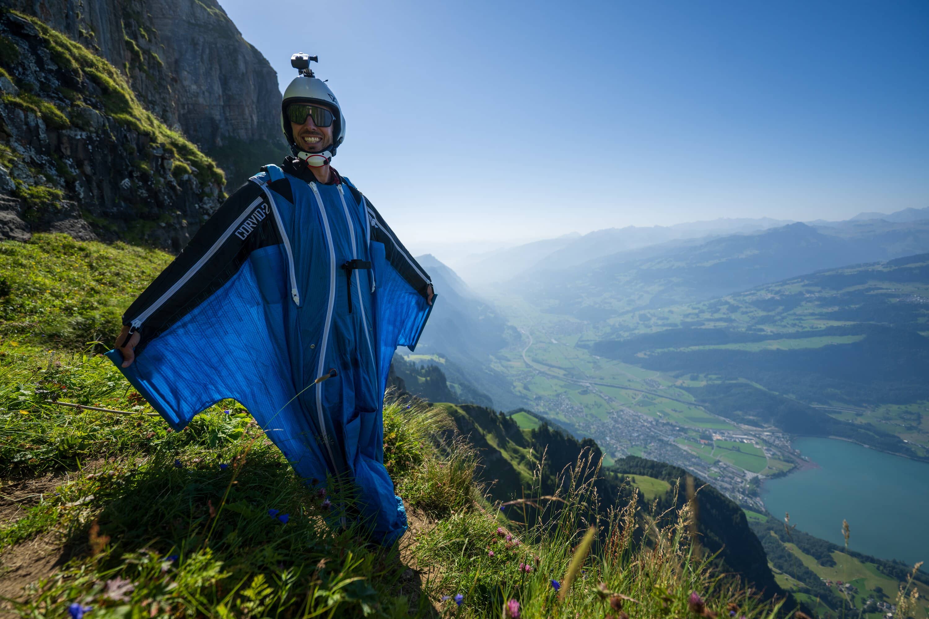 Marcel Geser steht in blauem Wingsuit oberhalb eines Sees