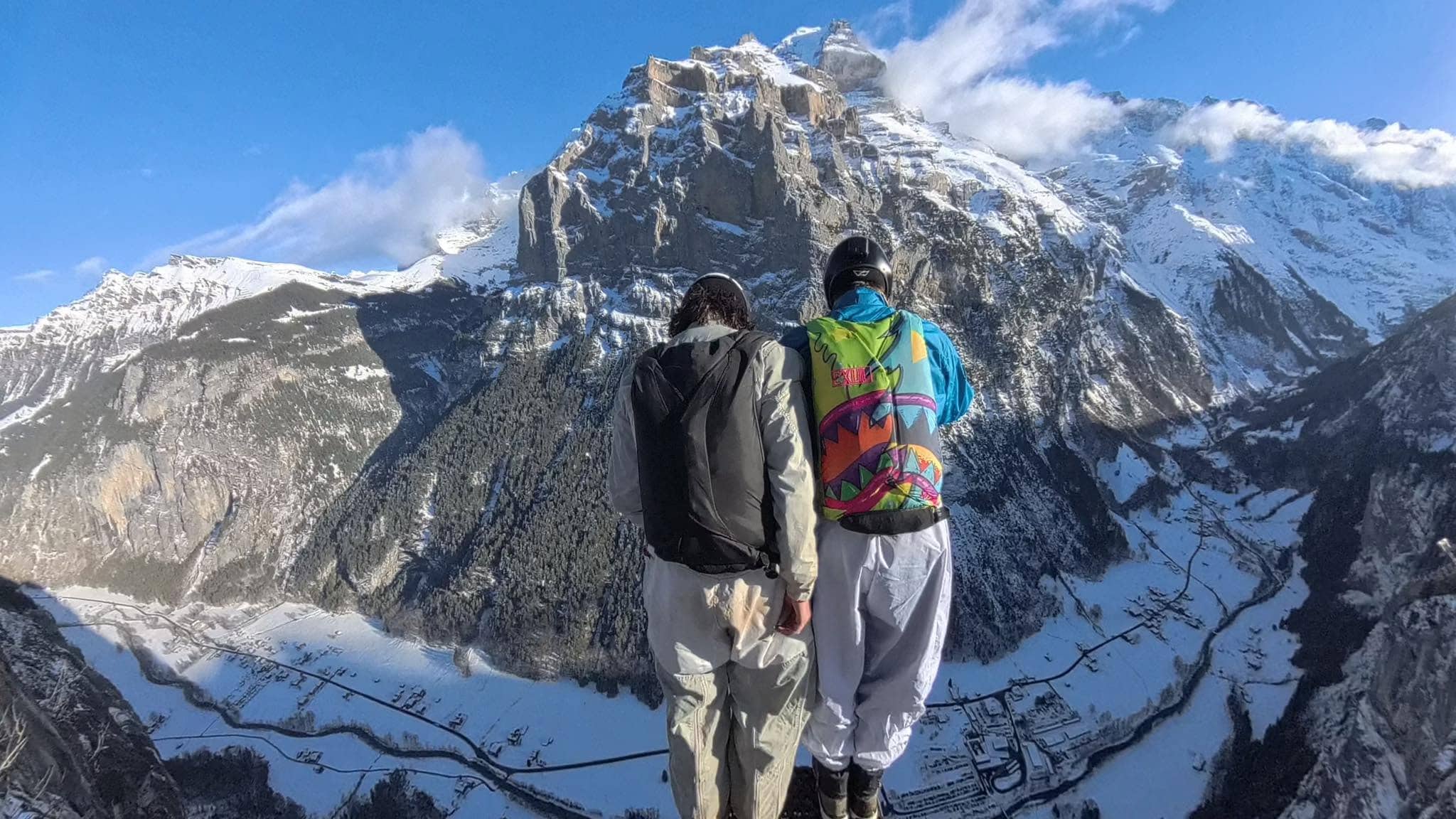 BASE Jumper in weissem Wingsuit über einem bewaldeten Tal