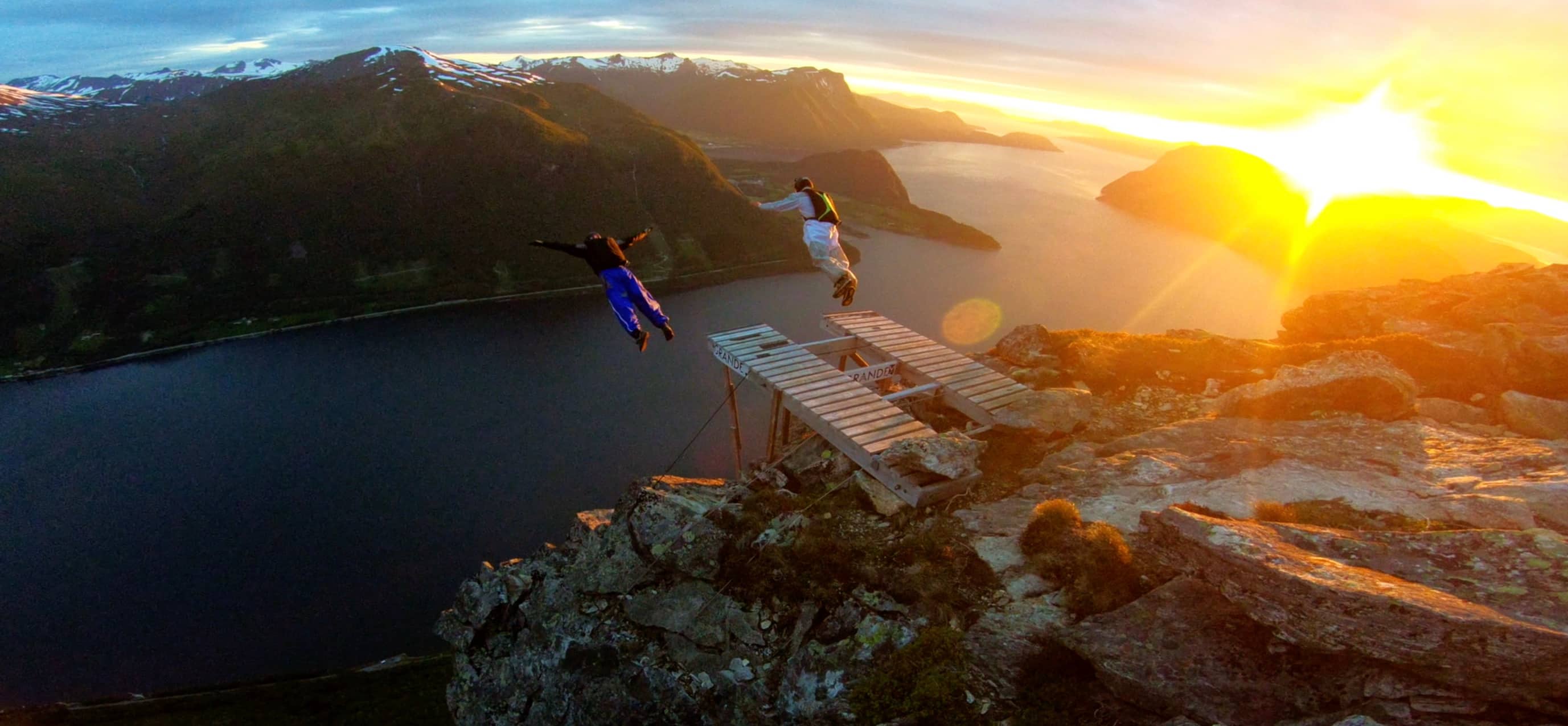 BASE Jumper in roter Jacke steht unter einer verschneiten Felswand