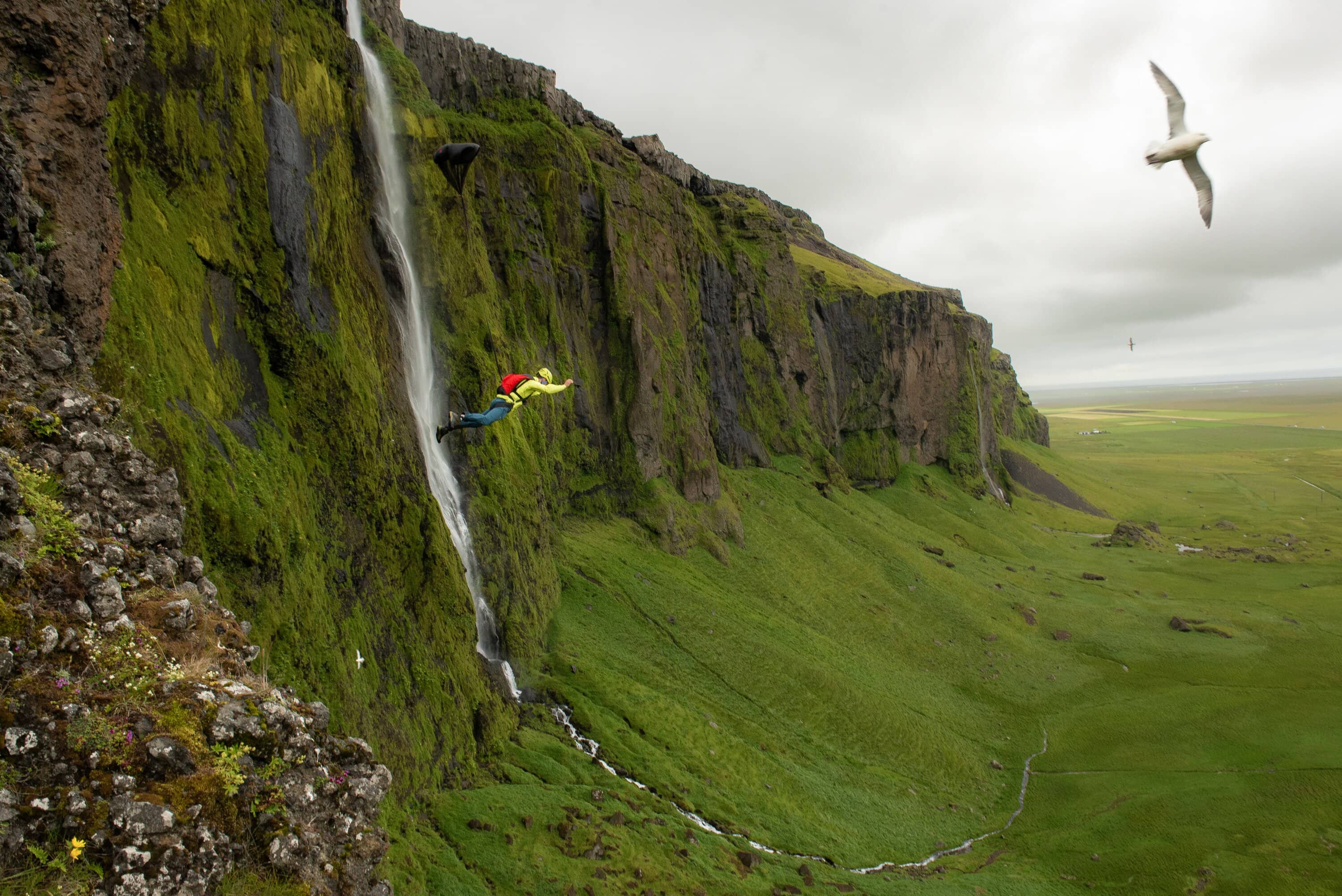BASE Jumper fliegt neben einer grünen Felswand mit Wasserfall