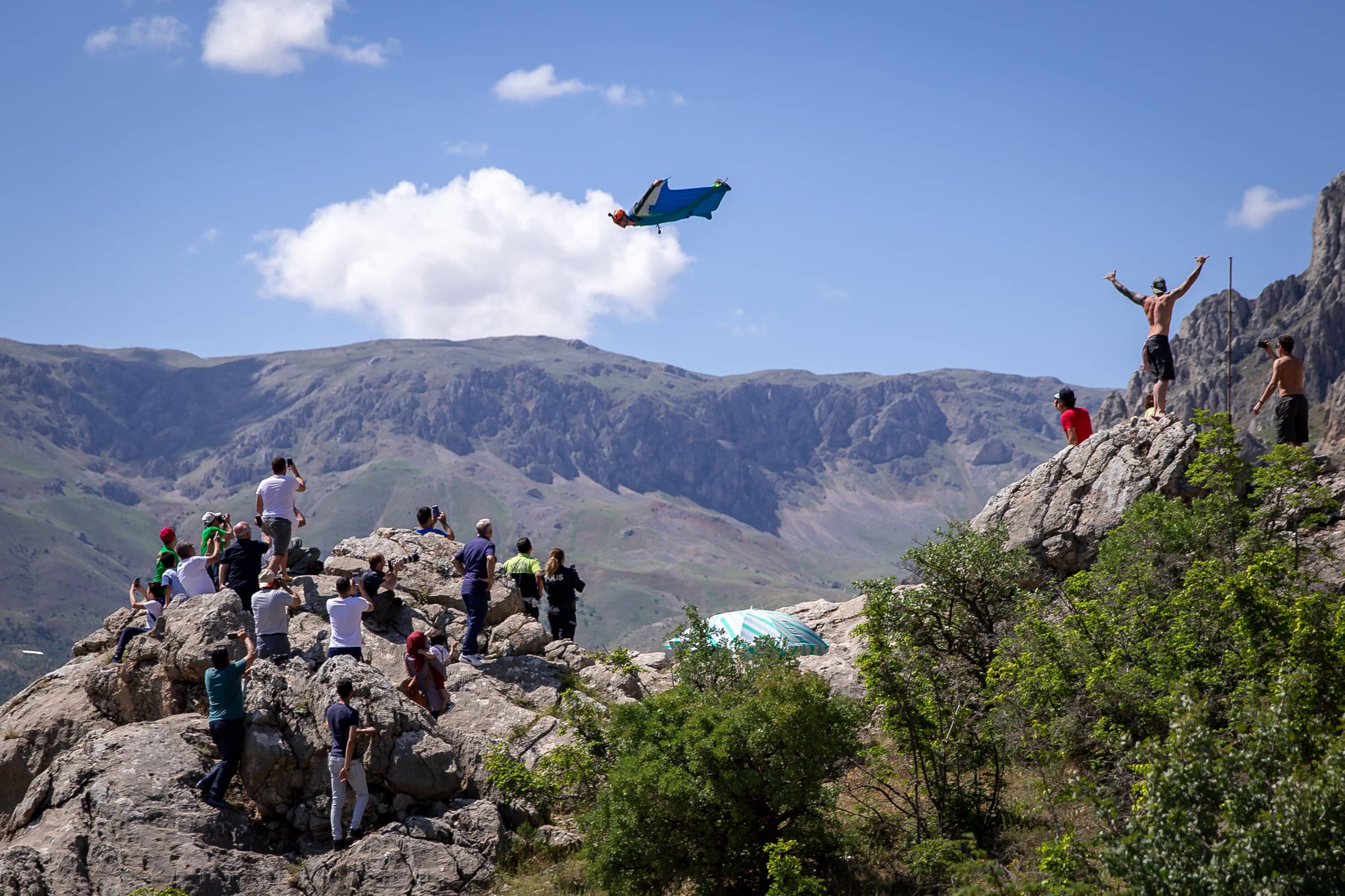 BASE Jumper fliegt über einem Felsgrat vor blauem Himmel