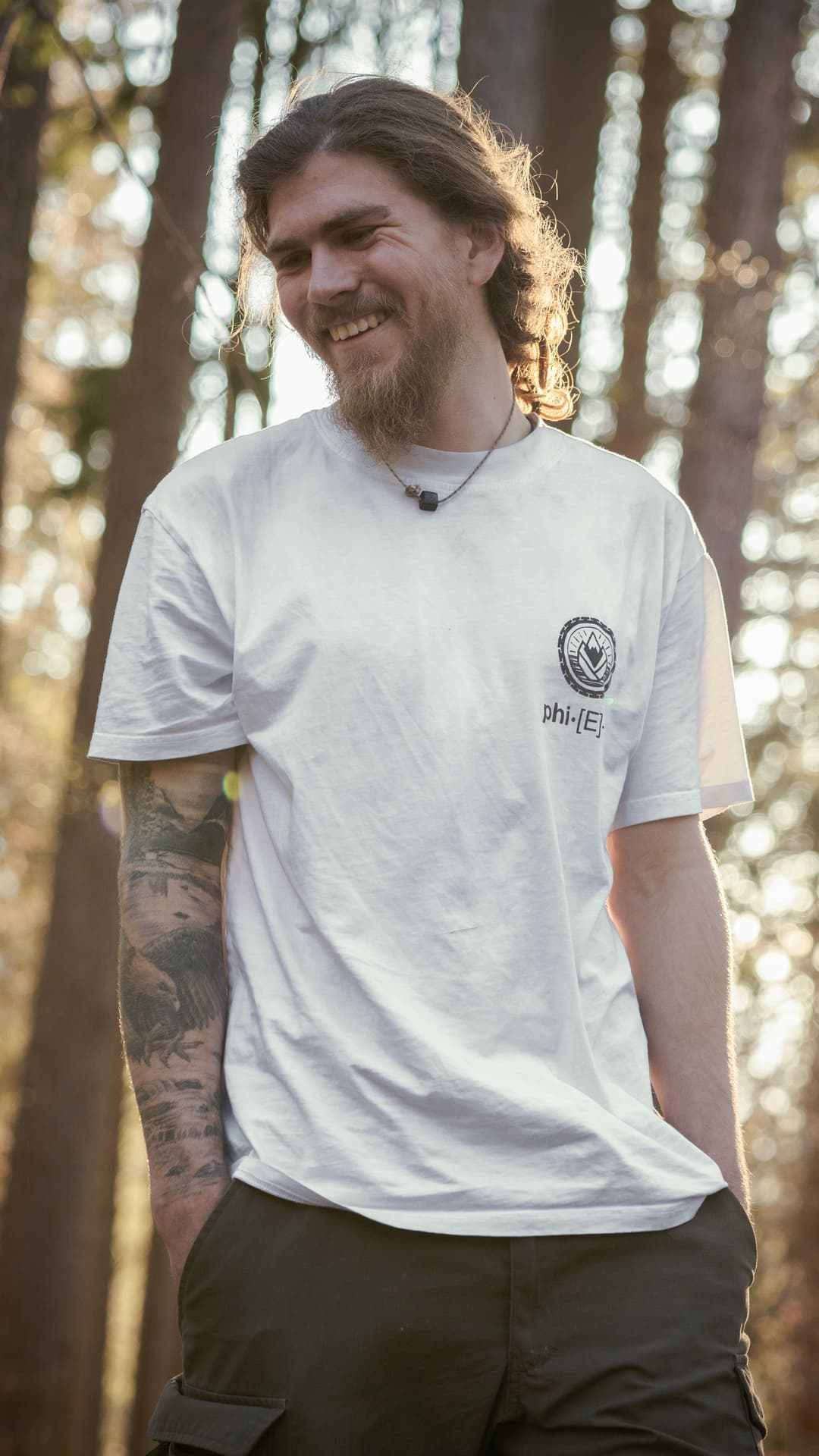 Lukas Loibl lächelt in einem weissen Shirt in einem sonnigen Wald