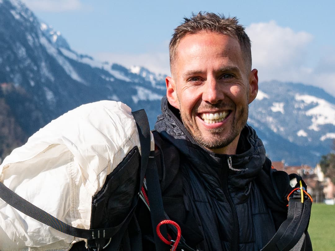 Marcel Geser lächelt mit seinem Fallschirm vor verschneiten Bergen