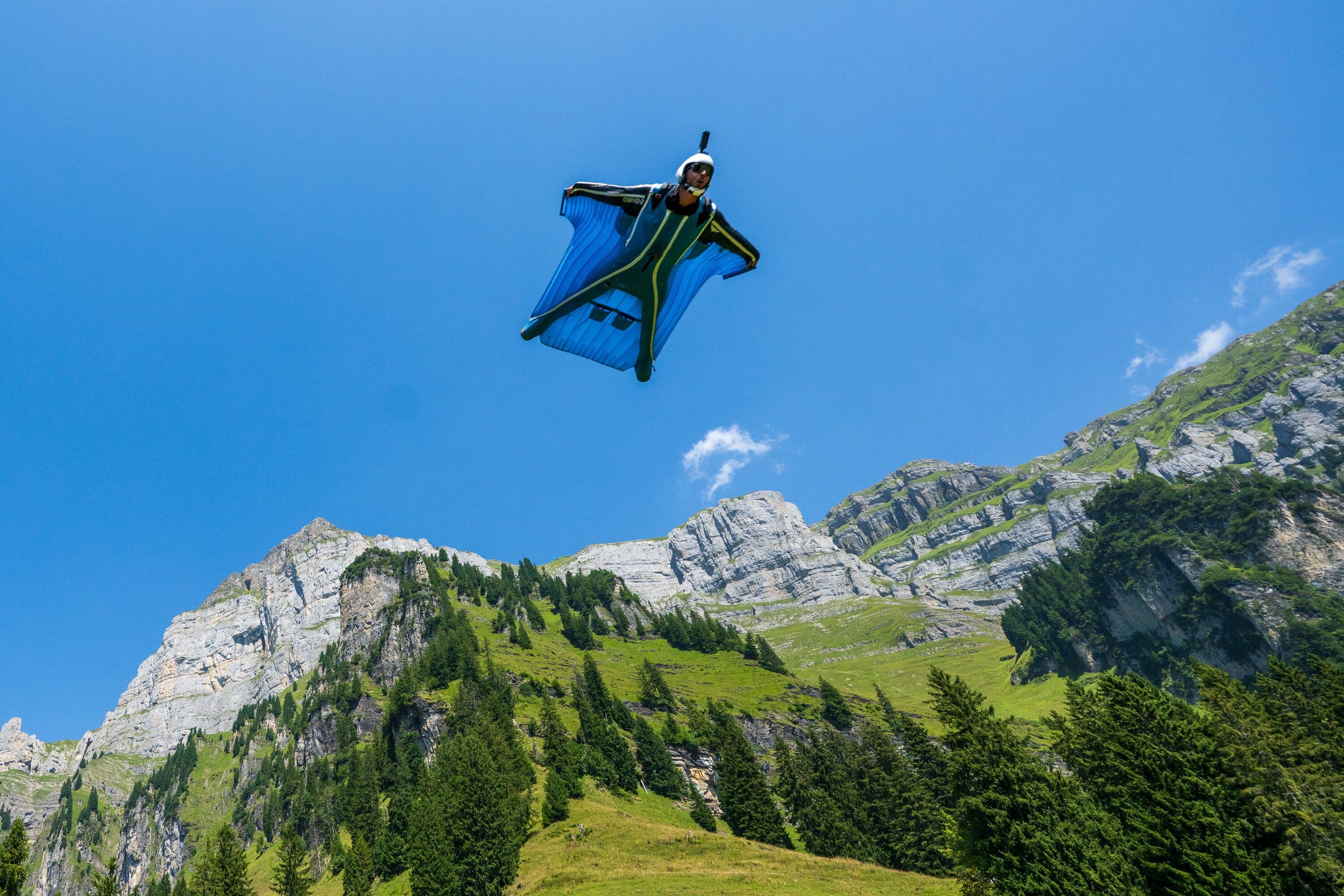 Wingsuit flyer gliding below a cliff under a blue sky