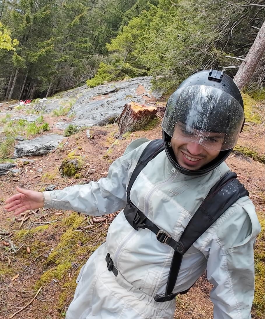 Niclas Strohmeier lächelt im weissen Wingsuit und Helm in einem Wald