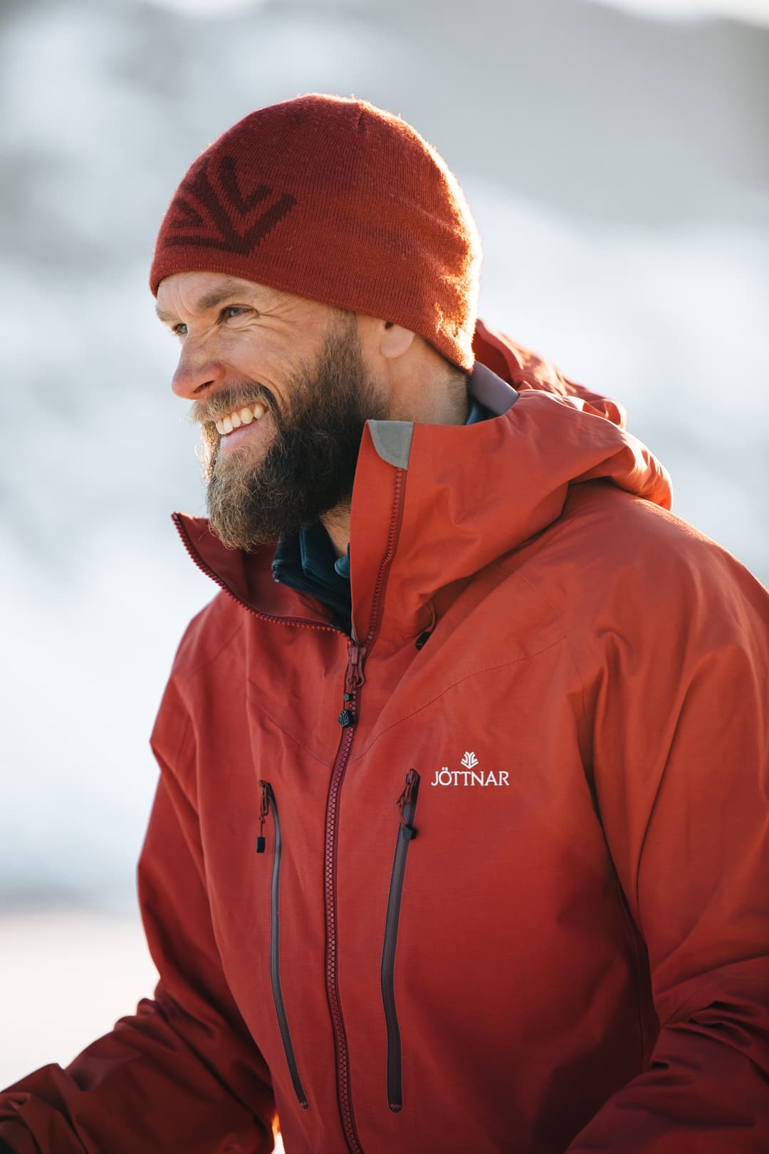 Tim Howell smiling in a red jacket and red beanie in snowy mountains