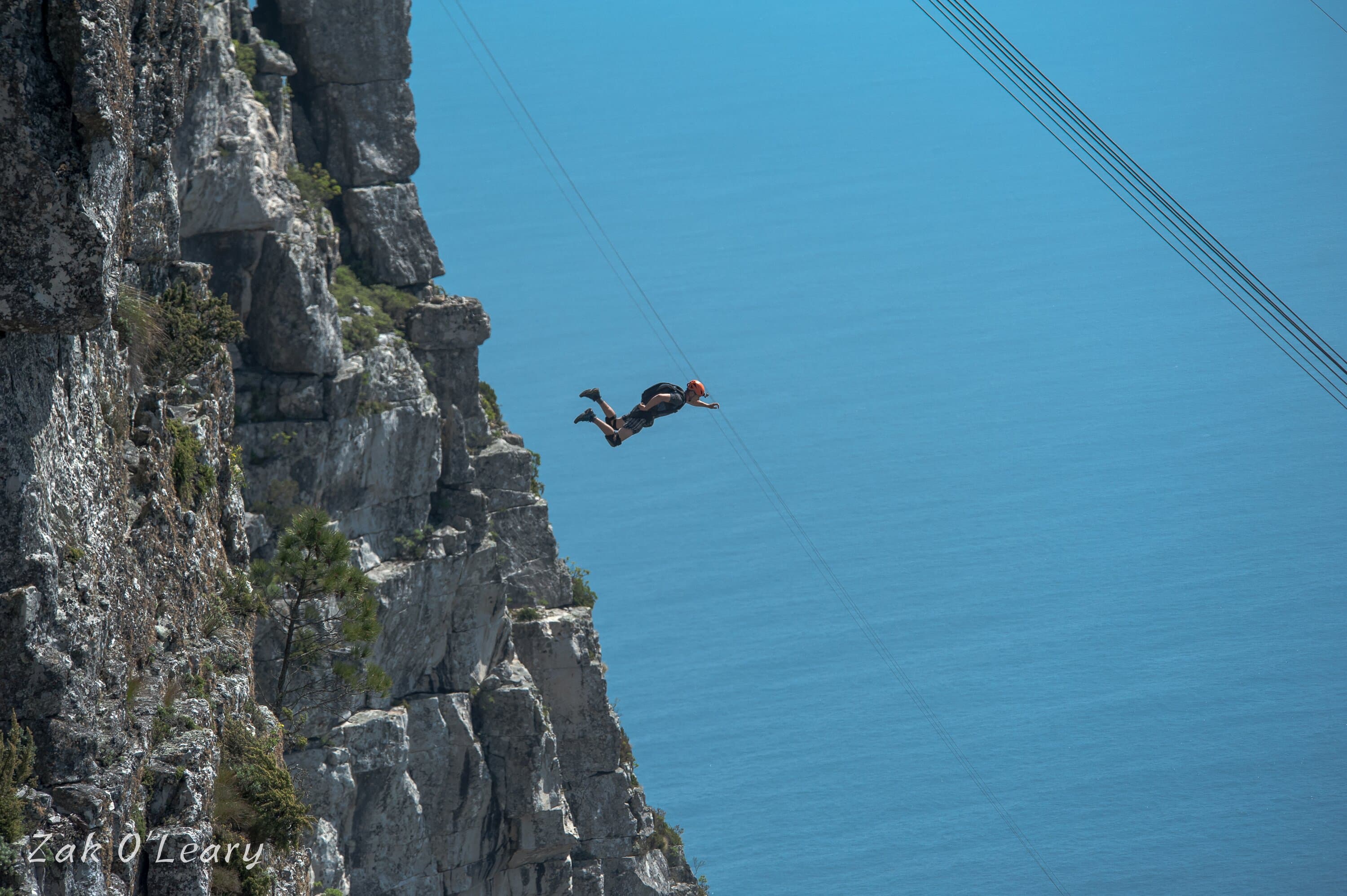 BASE jumper flying beside a cliff above deep blue water