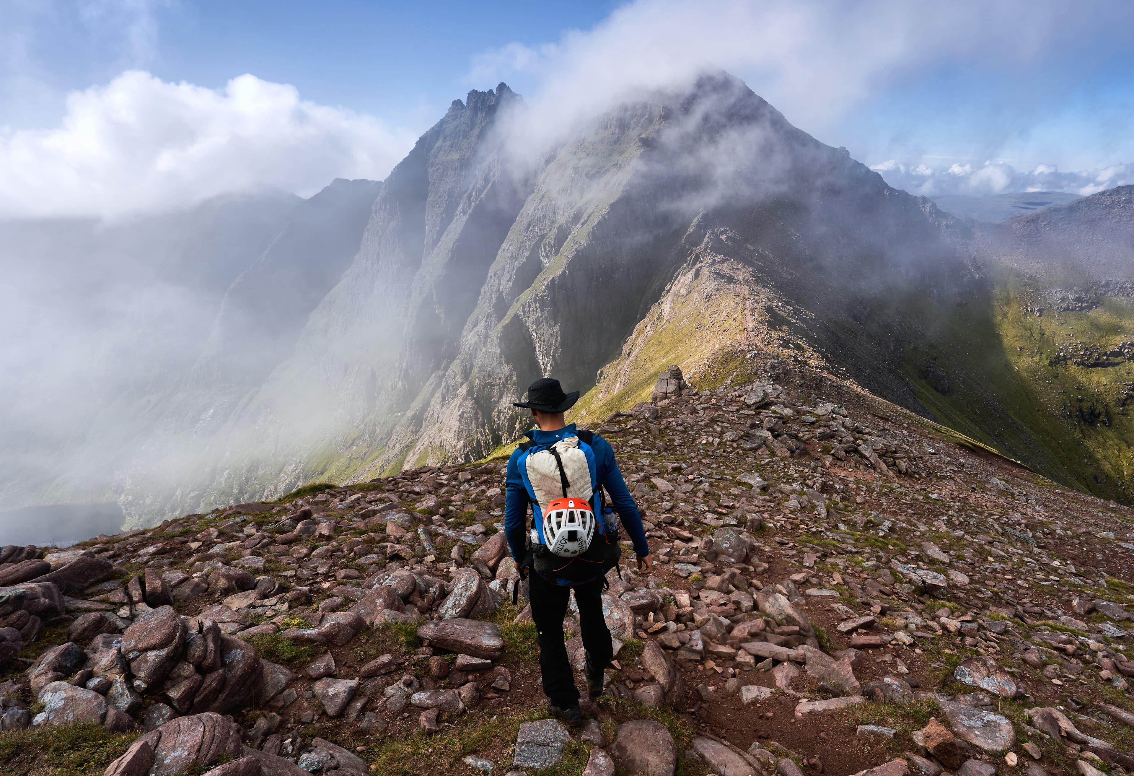 Ein BASE-Athlet steigt über einen felsigen Berggrat ab. Wolken ziehen über die umliegenden Gipfel und verdeutlichen die wechselnden Bedingungen.