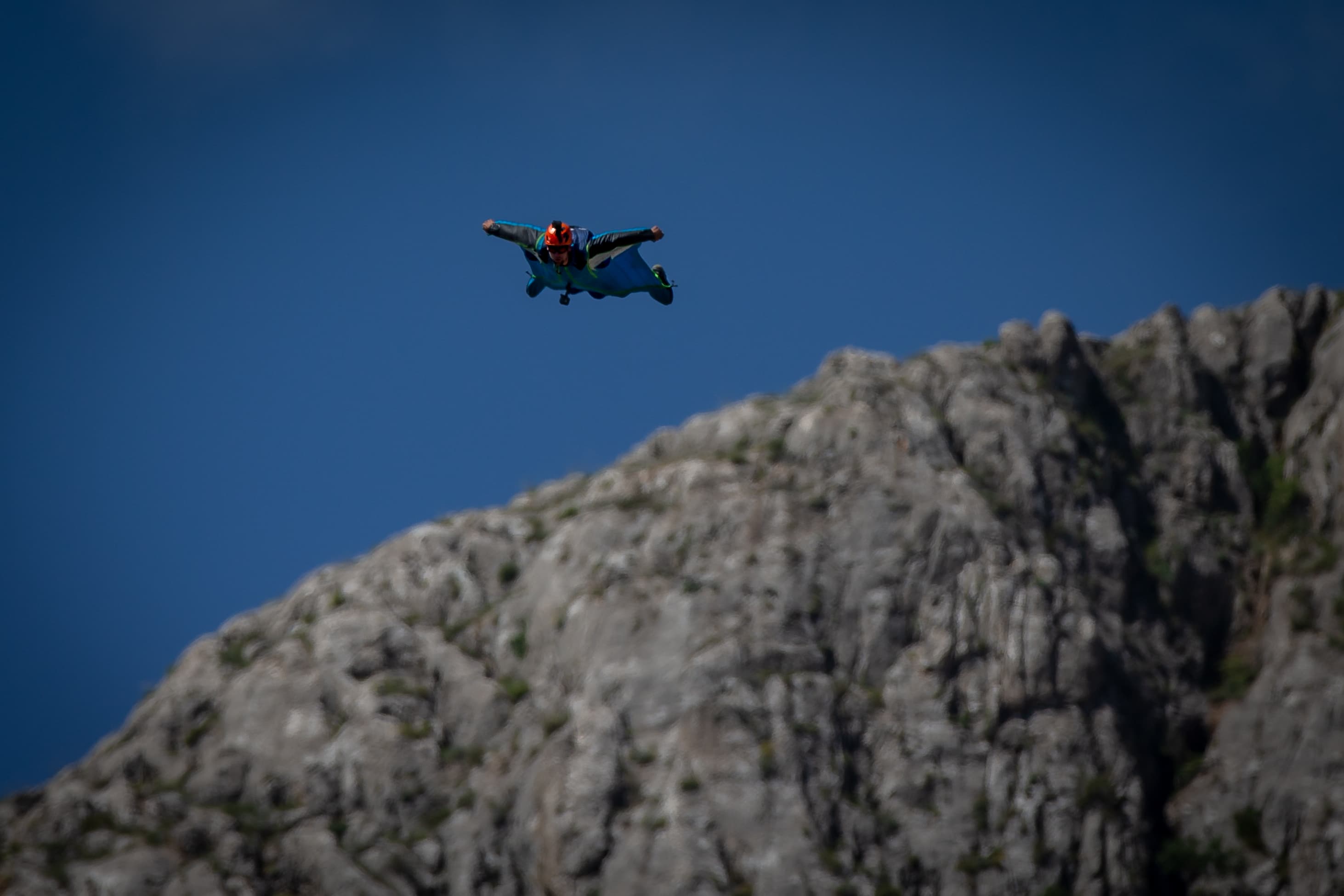 Ein BASE Jumper fliegt neben einer Felswand.