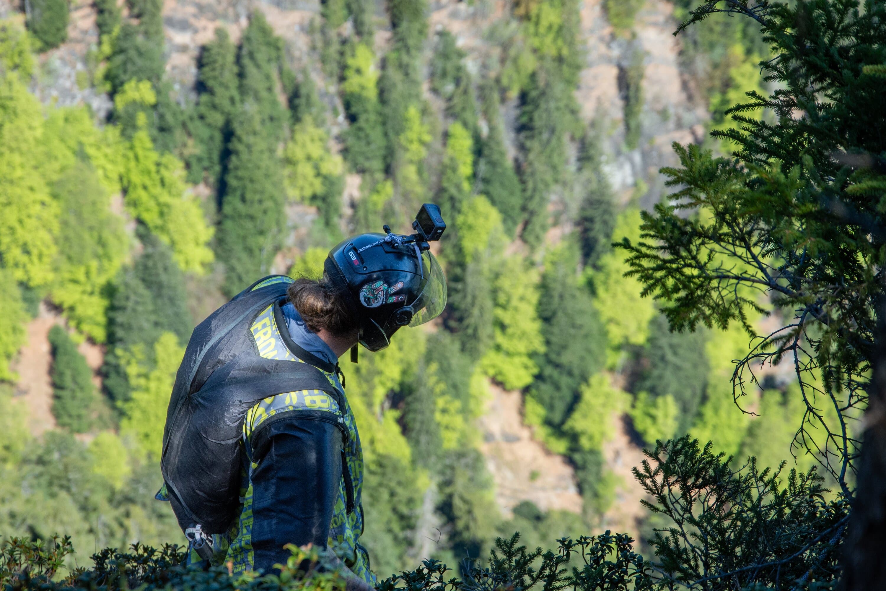 Person checking parachute gear above a green mountain valley