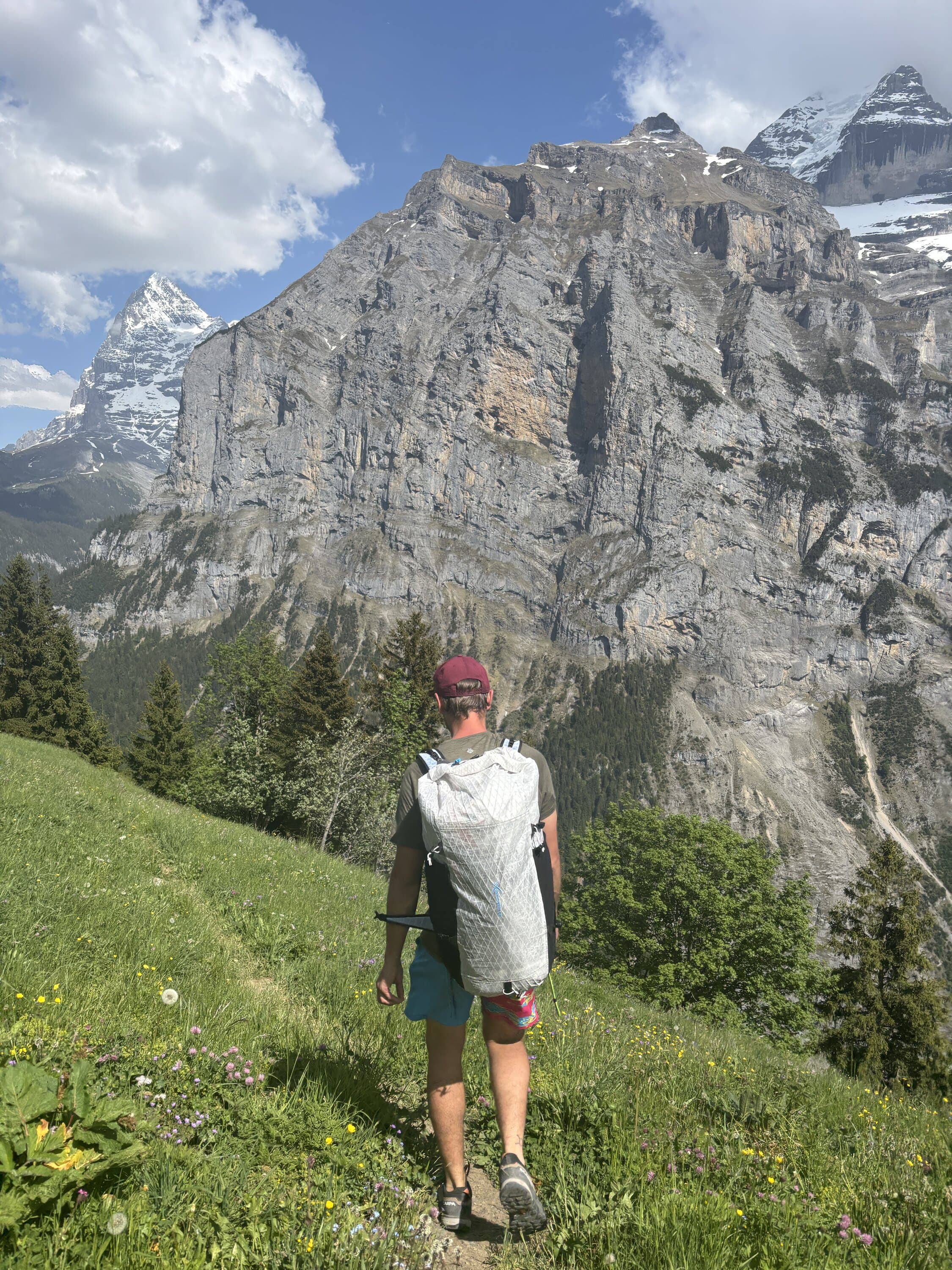 Person standing in a meadow below a rocky mountain face