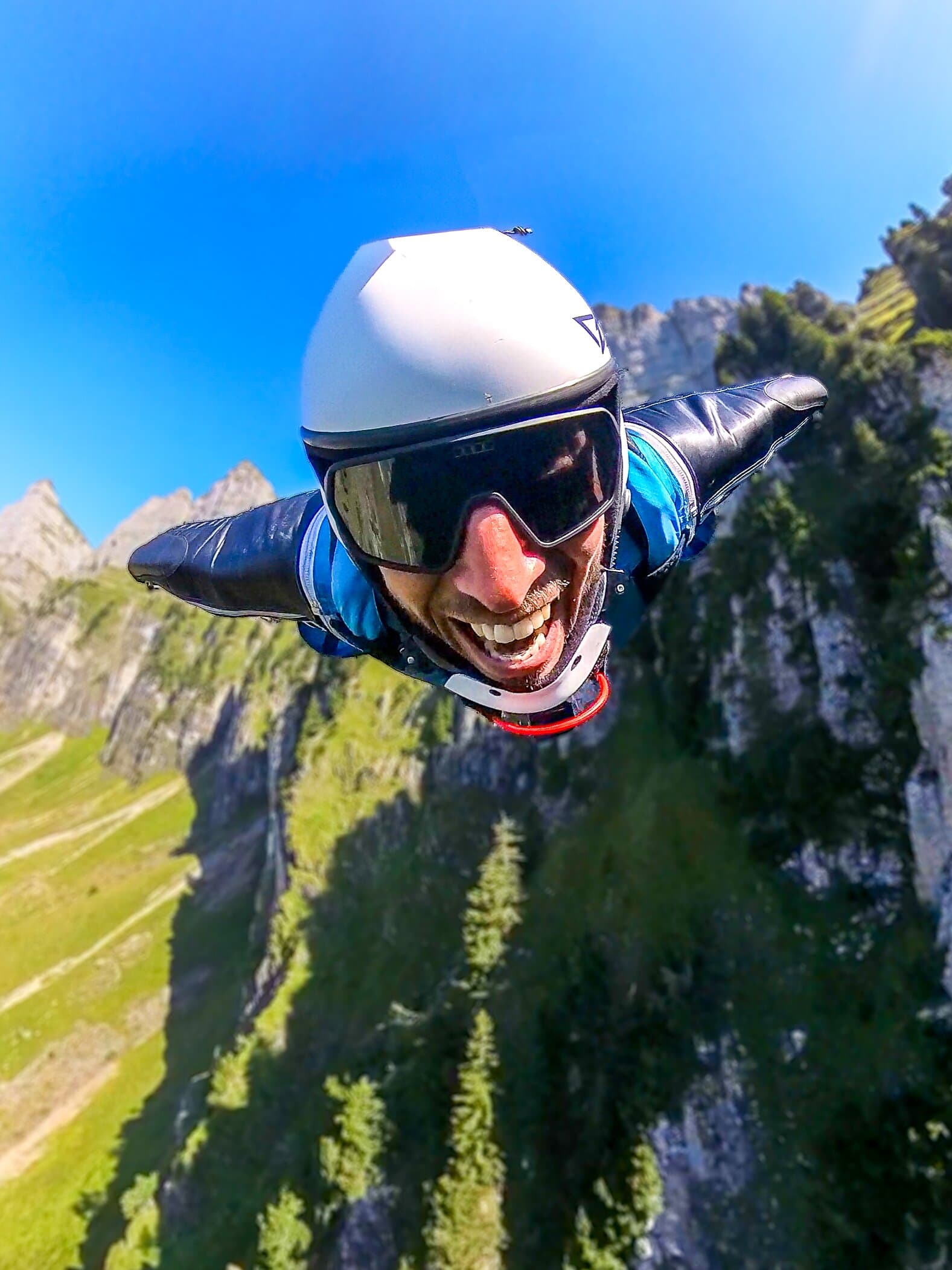 Marcel Geser flying in a blue wingsuit beside a green cliff