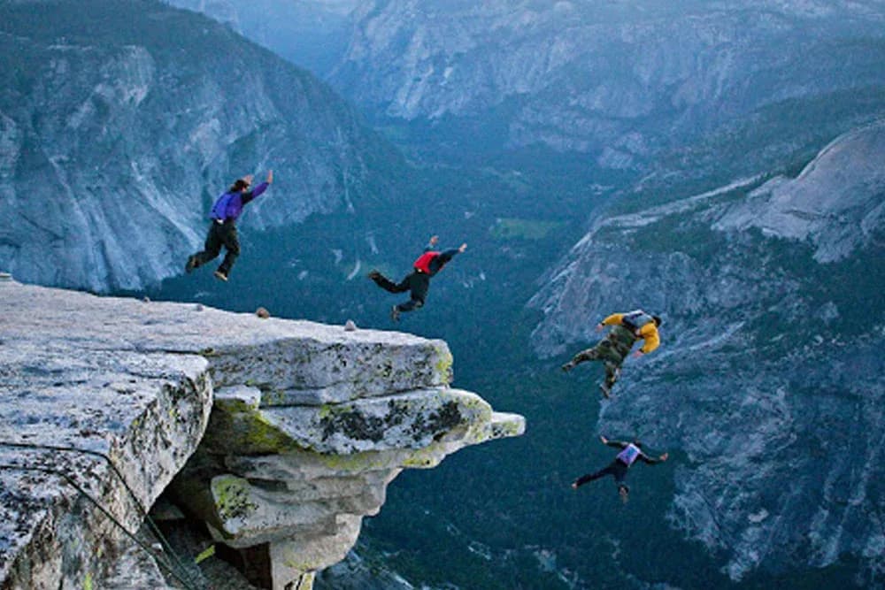 Several BASE jumpers exiting from a cliff above a valley.